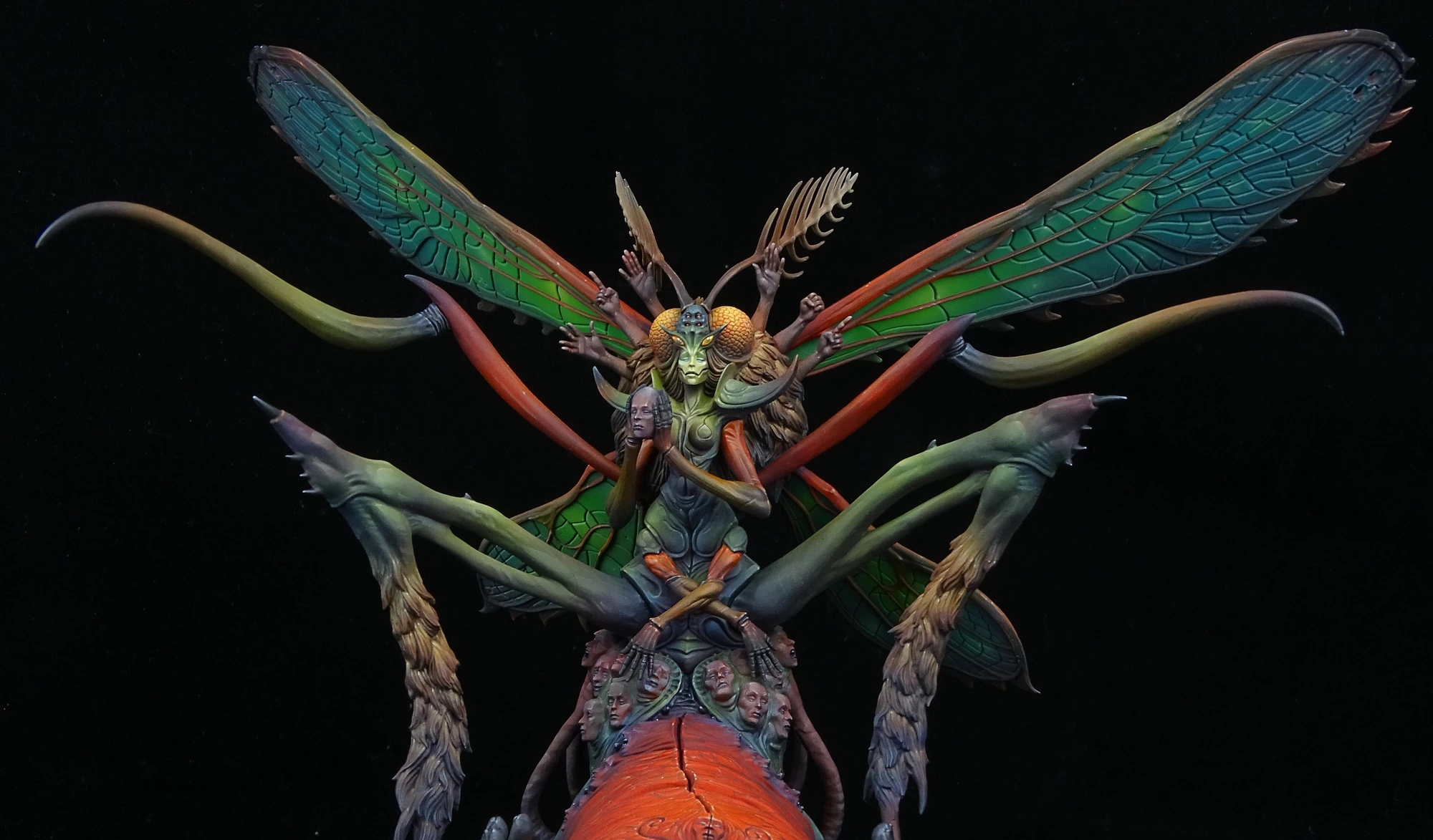 Painted moth-like fantasy creature with green and blue wings, sculpted faces and an orange body